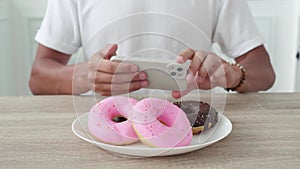 Unrecognizable man photographs donuts on a smartphone