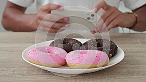 Unrecognizable man photographs donuts on a smartphone.