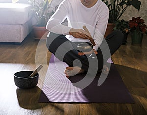 Unrecognizable man playing on singing bowl sitting on yoga mat in yoga class. Sound healing concept