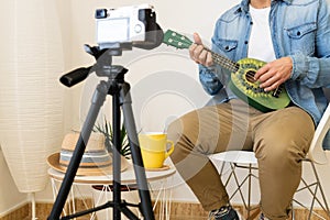 Unrecognizable man recording himself while playing on a green ukulele in a modern studio