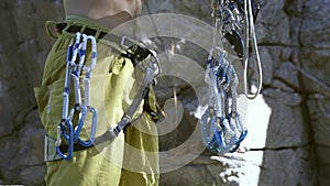 Unrecognizable man rock climber getting ready for outdoors climbing on cliff, and attaching quickdraws to the harness