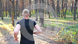 Unrecognizable man running along forest path. Male sportsman working out at nature. Athletic guy doing cardio training