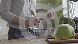 Unrecognizable man in the shirt cooking soup checking recipe on the tablet in the kitchen at home. Concept of healthy