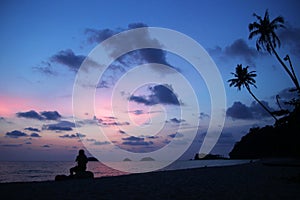 Unrecognizable man is sitting on the stones at the sunset on a sandy beach near to sea. Koh Chang, Thailand