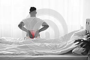 Unrecognizable Man Suffering Lower Back Pain While Sitting On Bed At Home