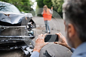 Unrecognizable man taking pictures of a broken car after an accident.
