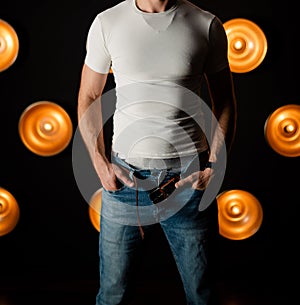 Unrecognizable man in a white T-shirt with unbuttoned jeans in a dark room