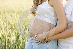 Unrecognizable married couple during pregnancy enjoys walk in nature on summer day, man hugs his wife& x27;s stomach.