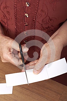 Unrecognizable mature woman cutting with scissors pieces of white cardboard