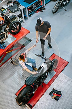 Unrecognizable mechanic giving tool to female coworker repairing motorbike on garaje photo