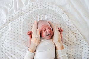 Unrecognizable mother caressing crying newborn baby son