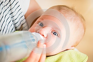 Unrecognizable mother feeding baby son, milk in bottle, close up