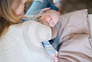 Unrecognizable mother holding sleeping baby son sitting on bed