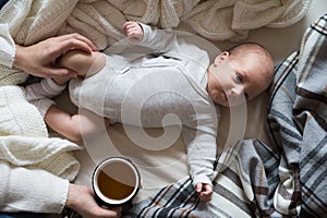 Unrecognizable mother with newborn baby son lying on bed