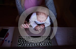 Unrecognizable mother with son on lap, working on laptop