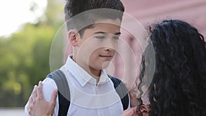 Unrecognizable mother woman brunette mommy correct collar on shirt of son stroking child on head talking to schoolboy