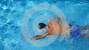 Unrecognizable muscular man swimming in clear blue water of pool. Young sporty guy floating across the basin of hotel on