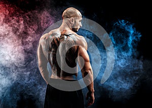 Unrecognizable muscular man with tattoo on back against of black background. Isolated.