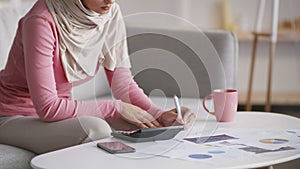 Unrecognizable muslim woman working at home, calculating finances and taking notes, making business plan, free space