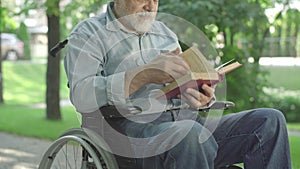 Unrecognizable paralyzed senior man turning book page and reading out loud. Old grey-haired male Caucasian retiree
