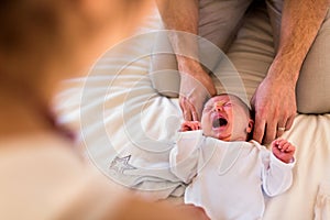 Unrecognizable parents at home dressing their baby girl on bed.