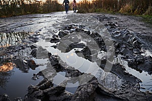 Unrecognizable pedestrians walk cautiously along the broken dirt road. The coating is slippery, wet, liquid