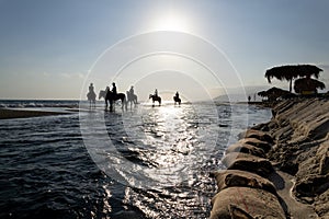 Unrecognizable people riding horses on the beach at dawn