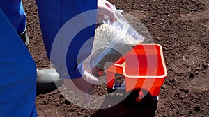 Unrecognizable person hands fill lawn grass seeds in plastic seeder device.