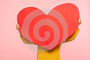 Unrecognizable person hiding behind large red paper heart, holding symbol of love affection fondness