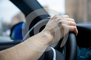 Unrecognizable person holds her right hand on the steering wheel and drives a modern car with a black interior. It`s a