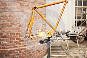 Unrecognizable person using a blowtorch to remove the paint of a bicycle frame