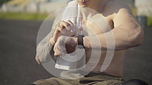Unrecognizable perspiring sportsman checking smart watch. Confident fit Caucasian man using online app for training