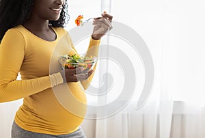 Unrecognizable pregnant black lady eating fresh salad, cropped