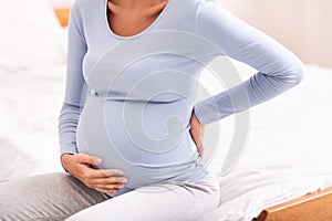 Unrecognizable Pregnant Woman Having Backache Sitting In Bed At Home