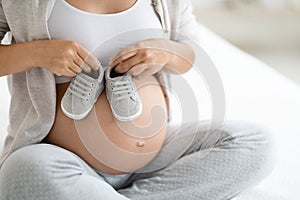 Unrecognizable pregnant woman holding baby shoes on her big belly