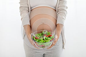 Unrecognizable pregnant woman holding bowl with fresh salad