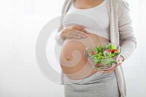 Unrecognizable pregnant woman holding bowl with fresh salad, copy space