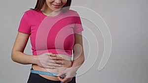 Unrecognizable pregnant woman measuring her belly with a measuring tape while standing on a white background. A pregnant