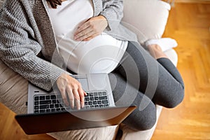 Unrecognizable pregnant woman relaxing on sofa and using laptop