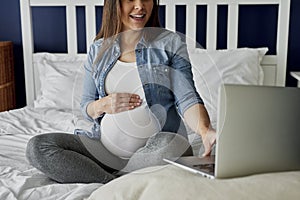 Unrecognizable pregnant woman using laptop in bed
