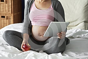 Unrecognizable pregnant woman using tablet while sitting in bed