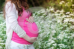 Unrecognizable pregnant women holding her belly. Summer nature.