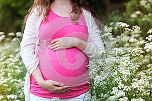 Unrecognizable pregnant women holding her belly. Summer nature.