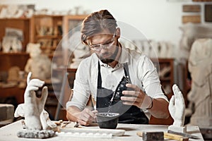 Unrecognizable professional stonemason with well-maintained hands making glue in special vessel for his handmade photo