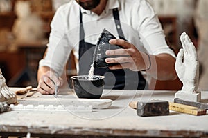 Unrecognizable professional stonemason with well-maintained hands making glue in special vessel for his handmade photo