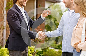 Unrecognizable real estate broker giving house key and shaking hands with new home owners near their property