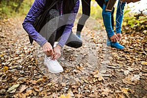 Unrecognizable runners in nature, tying shoelaces. Man with smar