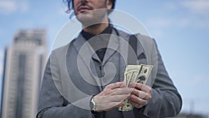 Unrecognizable satisfied businessman counting cash standing on city square outdoors. Young Caucasian man in elegant