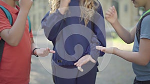 Unrecognizable schoolchildren playing rock-paper-scissors outdoors. three positive Caucasian pupils having fun on sunny