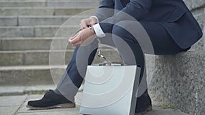 Unrecognizable secret agent sitting on urban stairs with attache case chained to his hand with handcuffs. Caucasian man